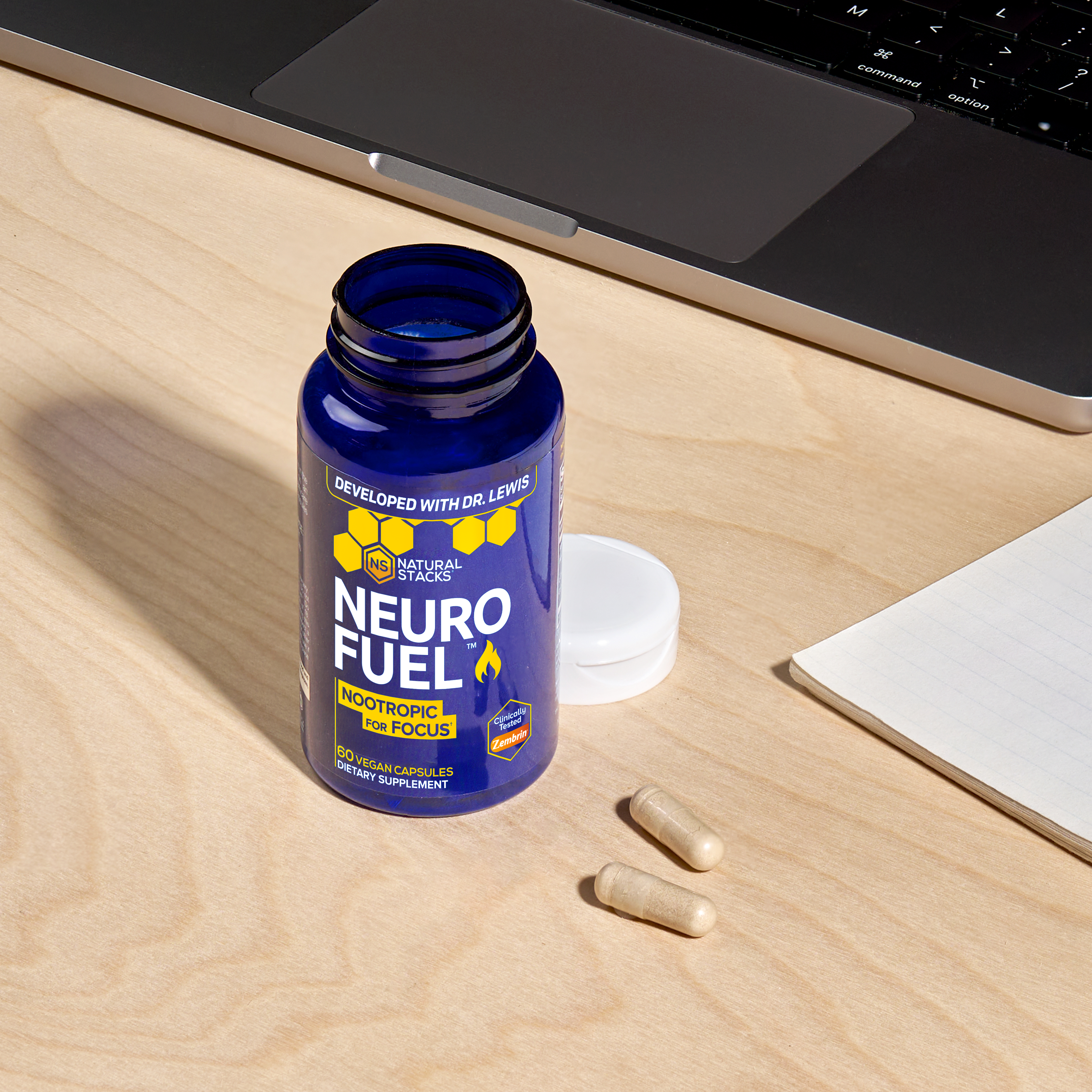 Open NeuroFuel bottle placed on a wooden table with two capsules beside it and the bottle cap positioned behind the bottle