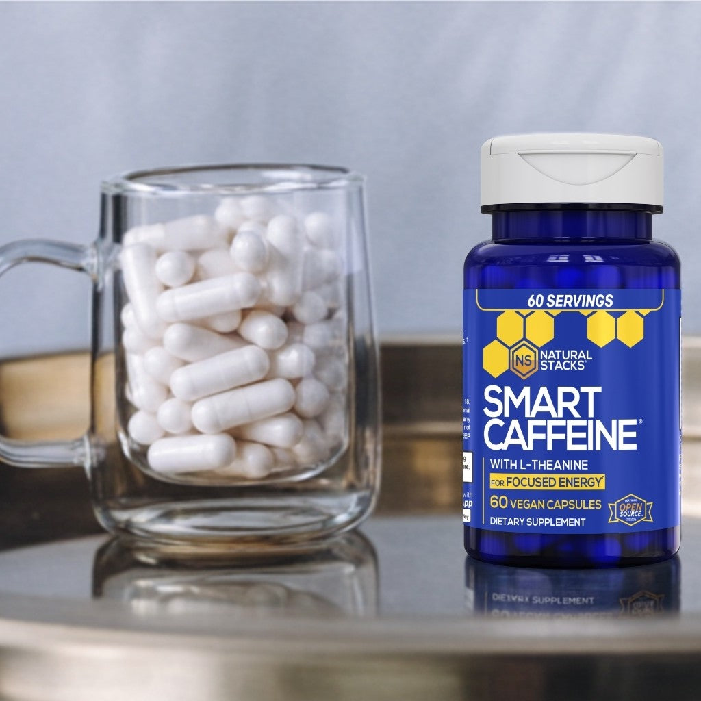 Supplement bottle labeled 'Smart Caffeine' next to a glass mug filled with capsules on a reflective surface.
