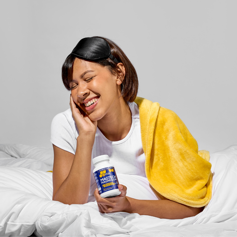 Woman in bed holding a bottle of supplements with a yellow towel draped over her shoulder.