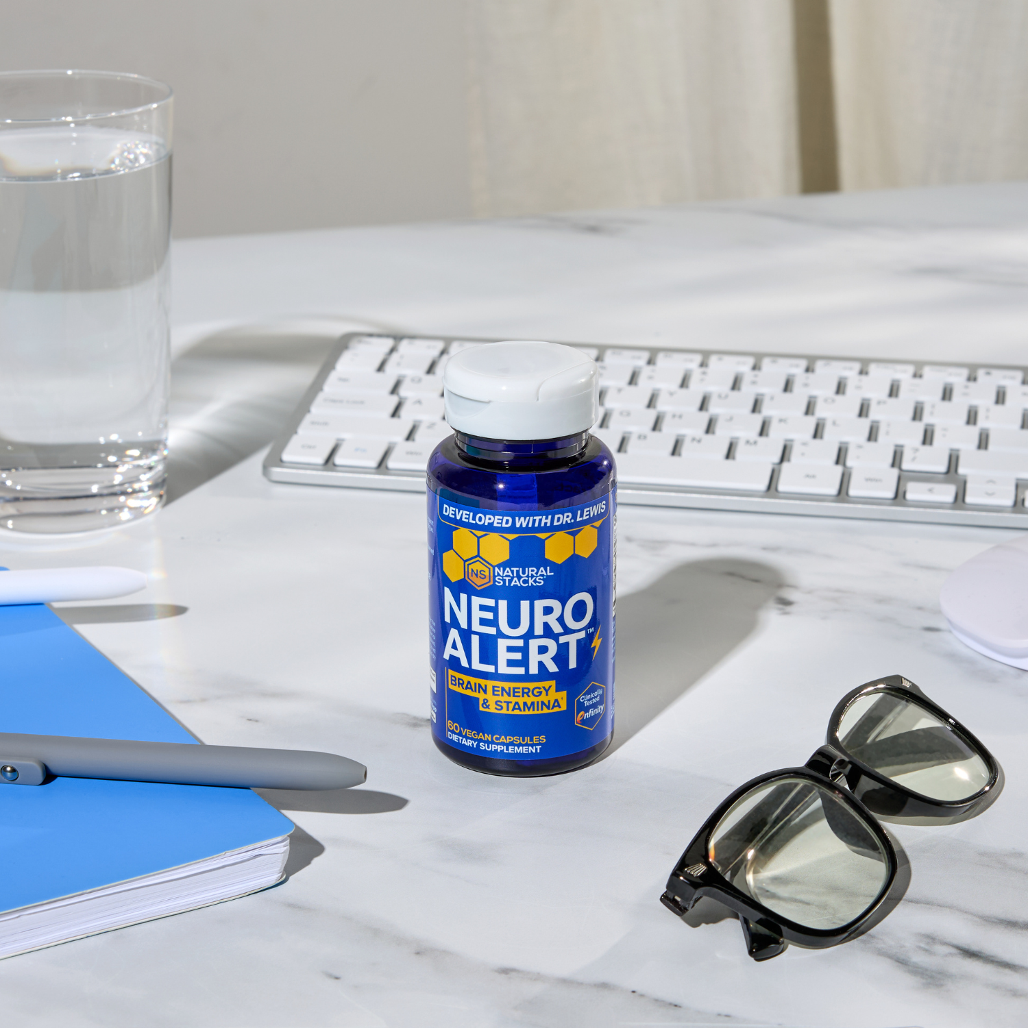 Neuro Alert supplement bottle on a desk with a keyboard, glasses, and water glass.