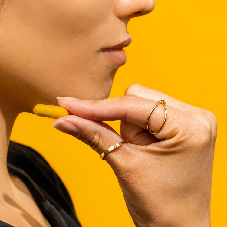 Profile of a woman holding a capsule close to her face against a bright yellow background.