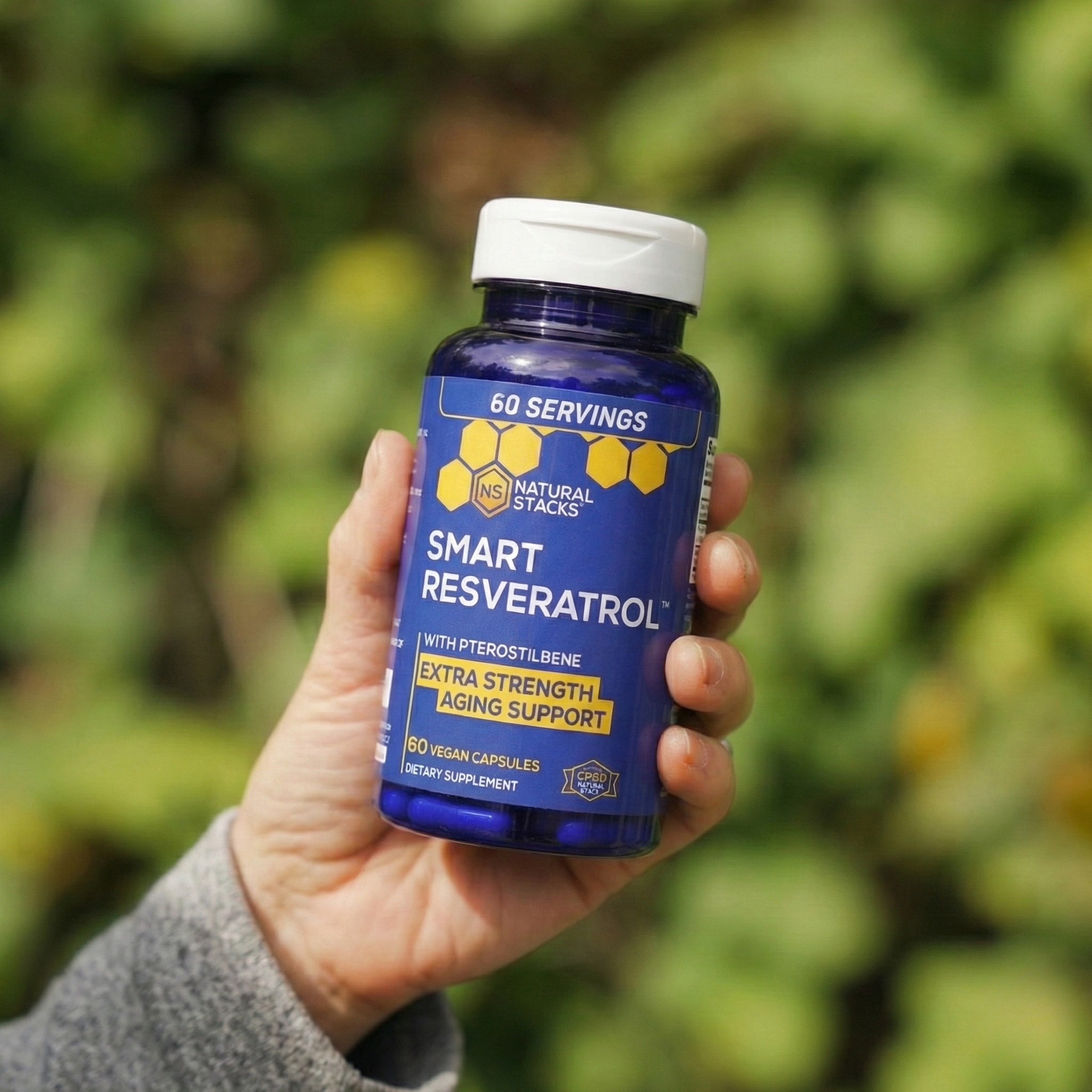 Hand holding a bottle of Smart Resveratrol supplement with a blurred green background