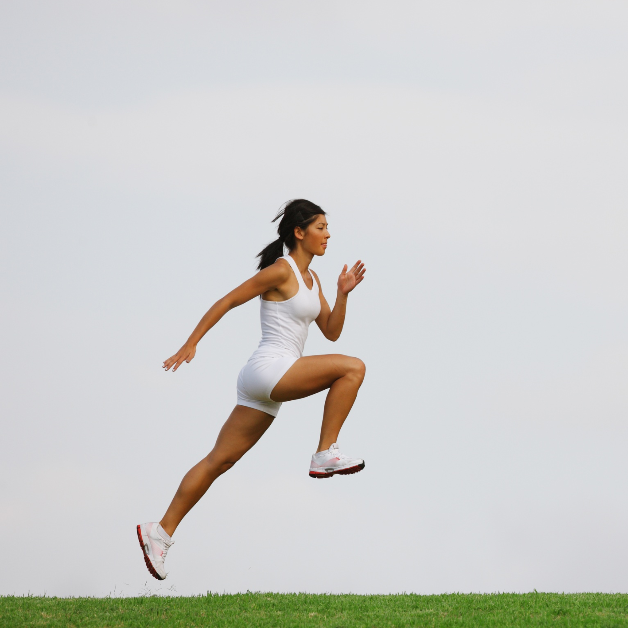 Woman in a white outfit running on grass with a clear sky background